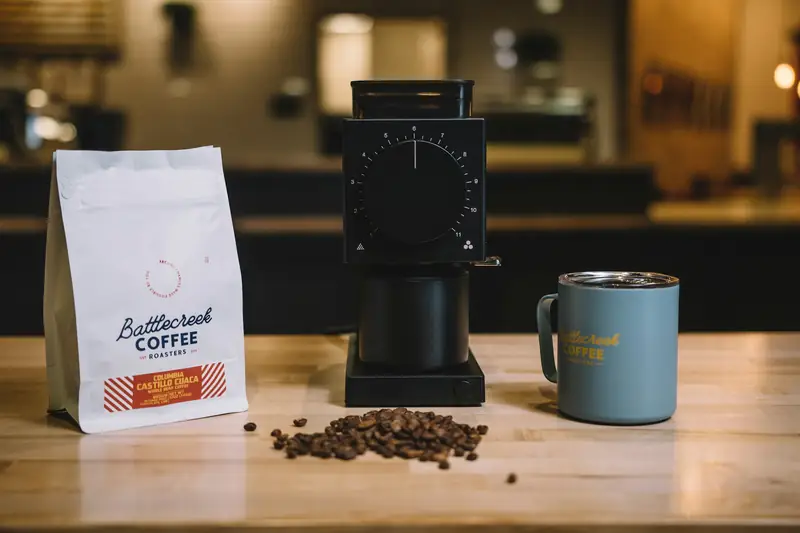 Branded coffee bag beside a coffee grinder and mug