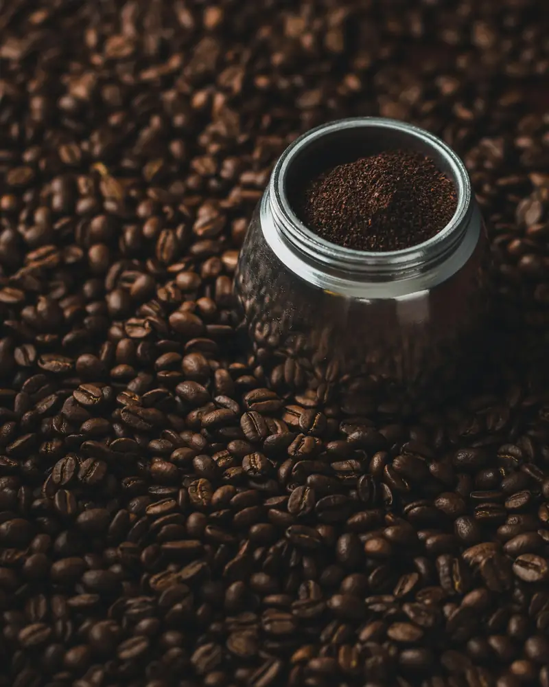 Freshly ground coffee in a cup surrounded by roasted beans