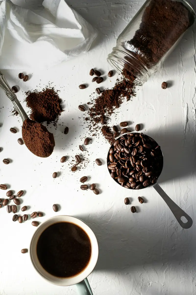 Ground coffee, whole beans and a cup of black coffee seen from above