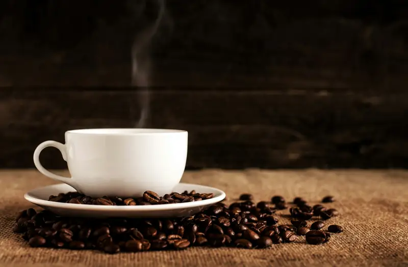 Steaming white cup of coffee resting on freshly roasted coffee beans